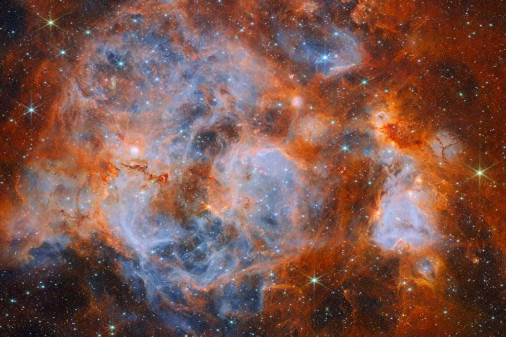 Imagen infrarroja de la nebulosa N159 captada por el telescopio James Webb, con nubes azuladas y anaranjadas y estrellas brillantes.