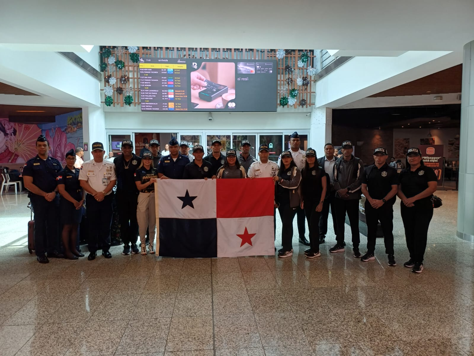 Delegación junto a una bandera de Panamá en una terminal aeroportuaria.