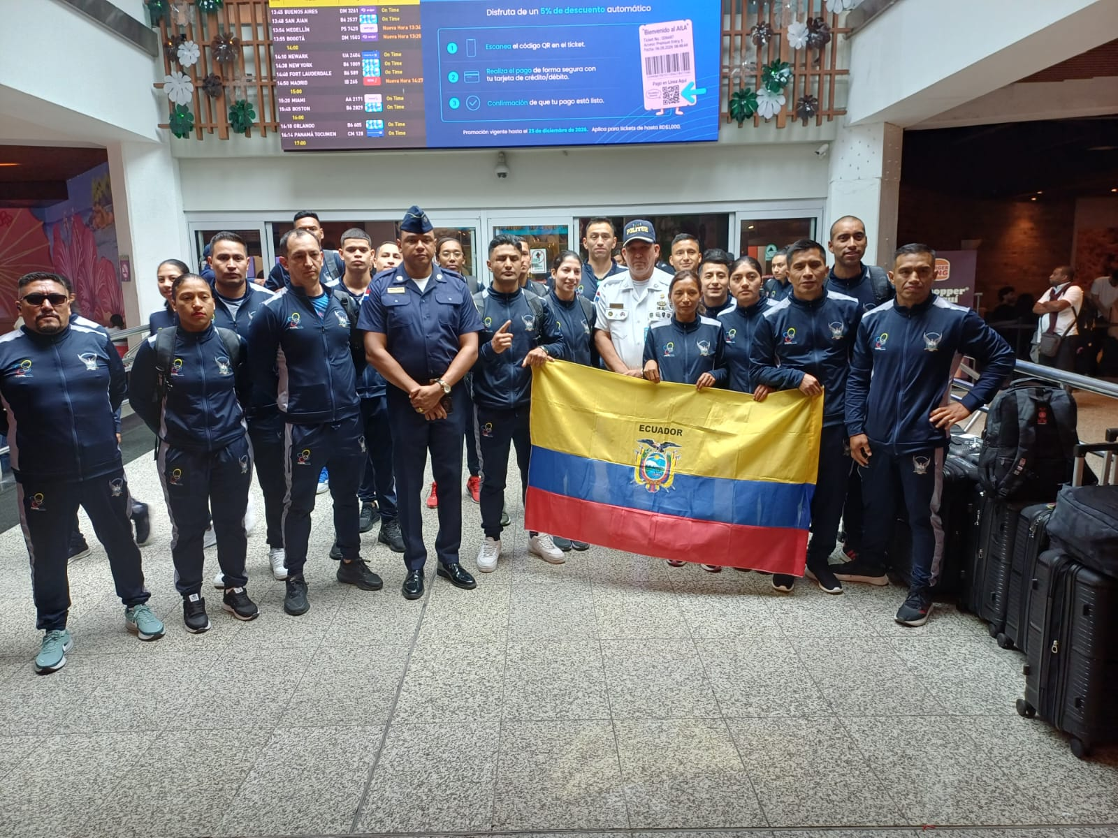 Delegación junto a una bandera de Ecuador en una terminal aeroportuaria.