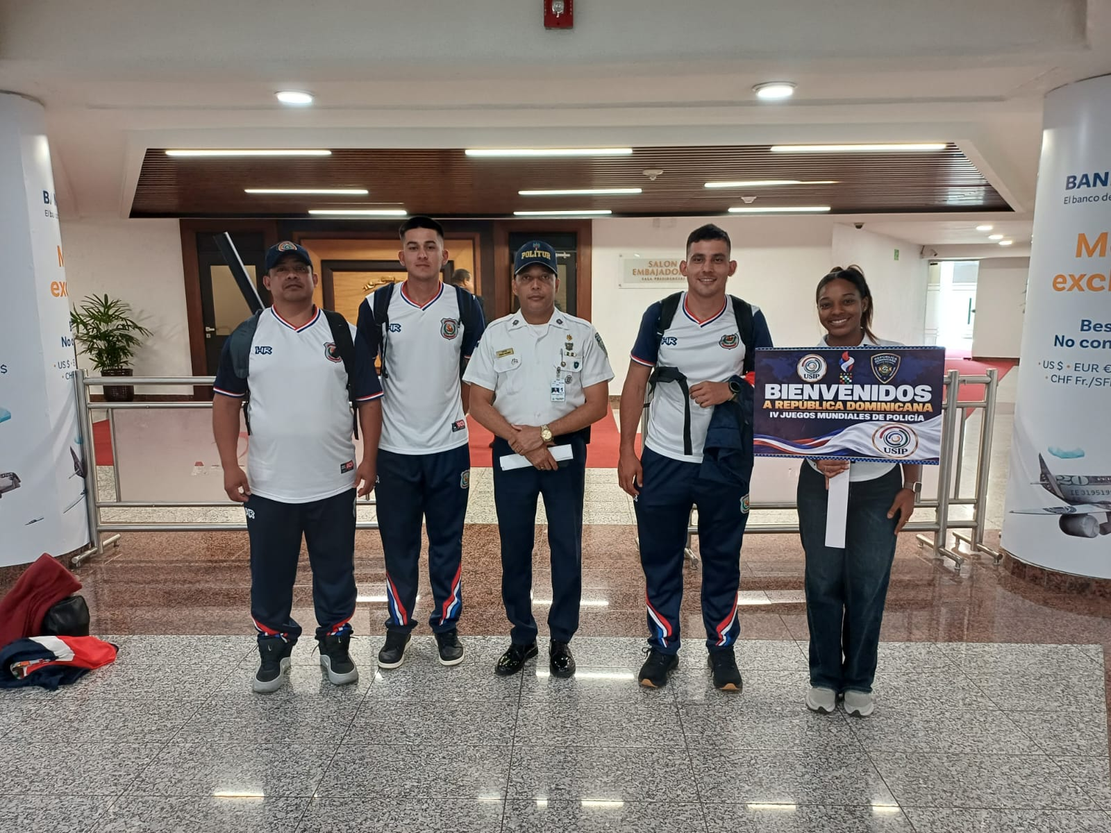 Personal deportivo posa con un letrero de bienvenida en el aeropuerto.