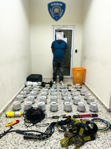 Medidores eléctricos y herramientas ocupados durante allanamiento policial en La Vega, con detenido de rostro cubierto